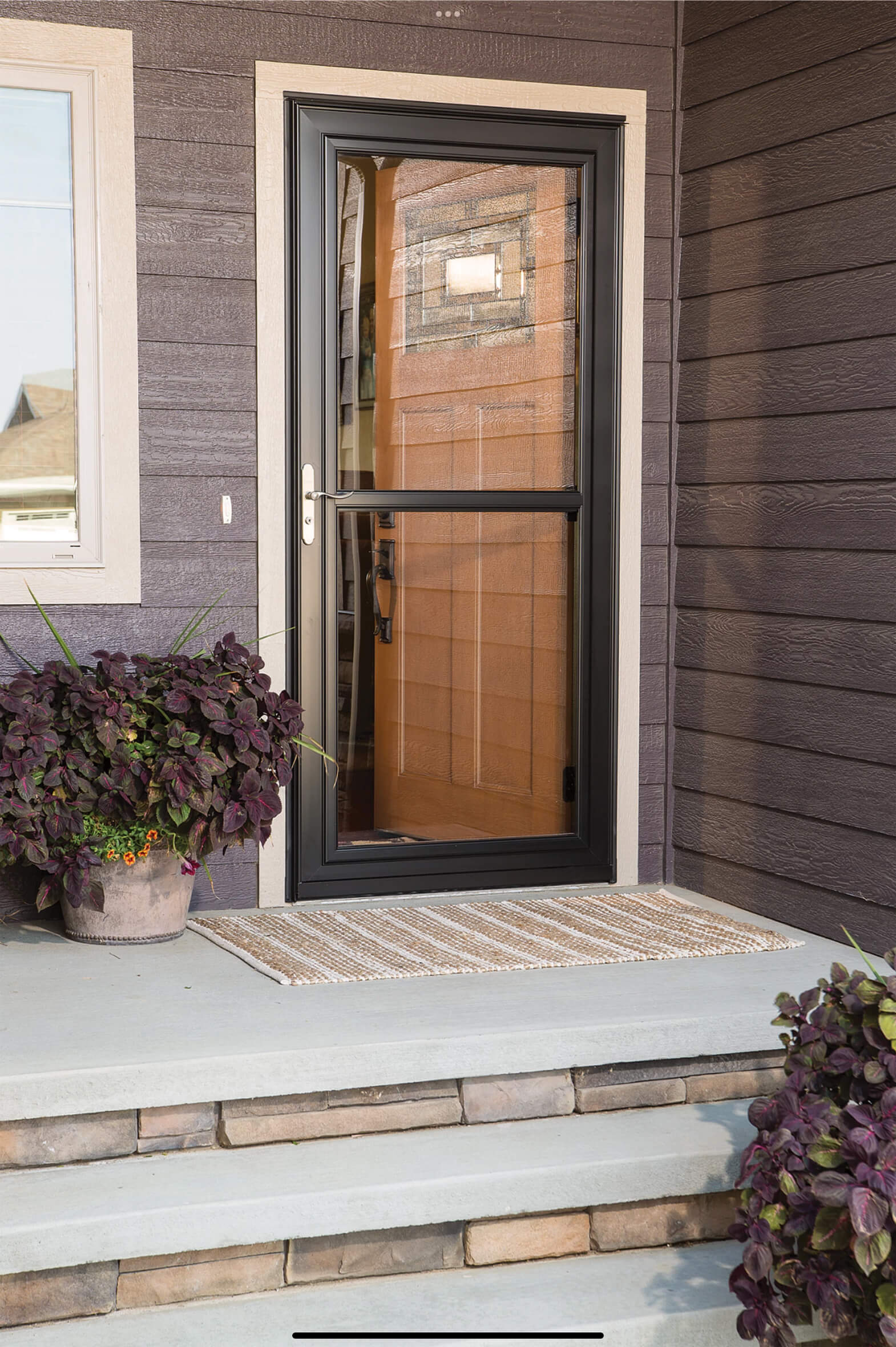 black-full-view-glass-storm-door-on-french-entry-door Black full-view glass storm door installed over a wood-grain French entry door with decorative glass panel