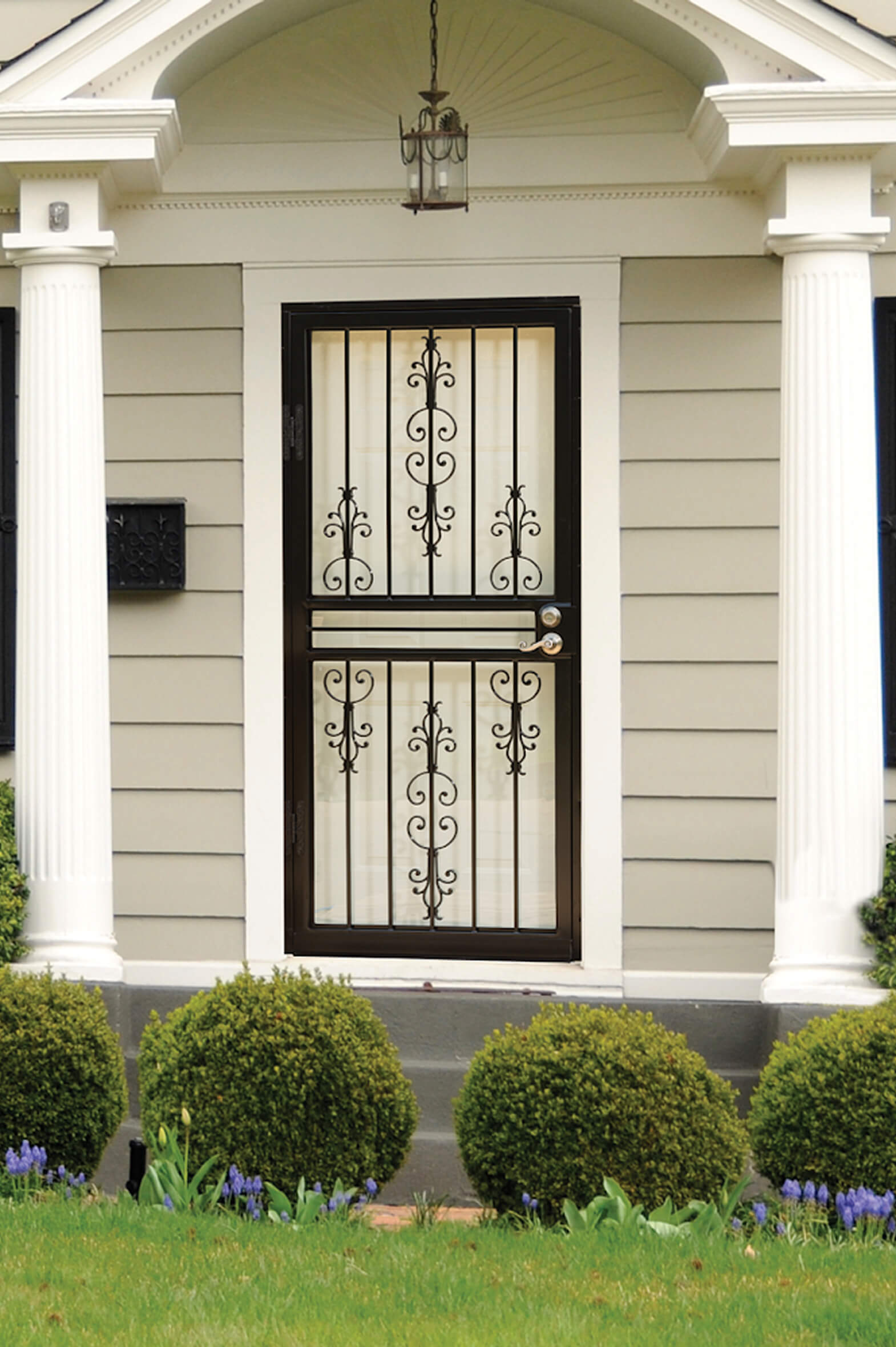 bronze-security-storm-door-scrollwork-white-columns Bronze security storm door with ornate scrollwork glass panels between white columns and boxwood shrubs