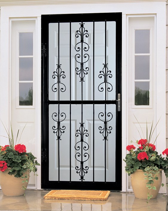 custom-fit-wrought-iron-security-screen-door Black wrought iron security screen door with decorative scrollwork installed over a white entry door, flanked by sidelights and red geraniums
