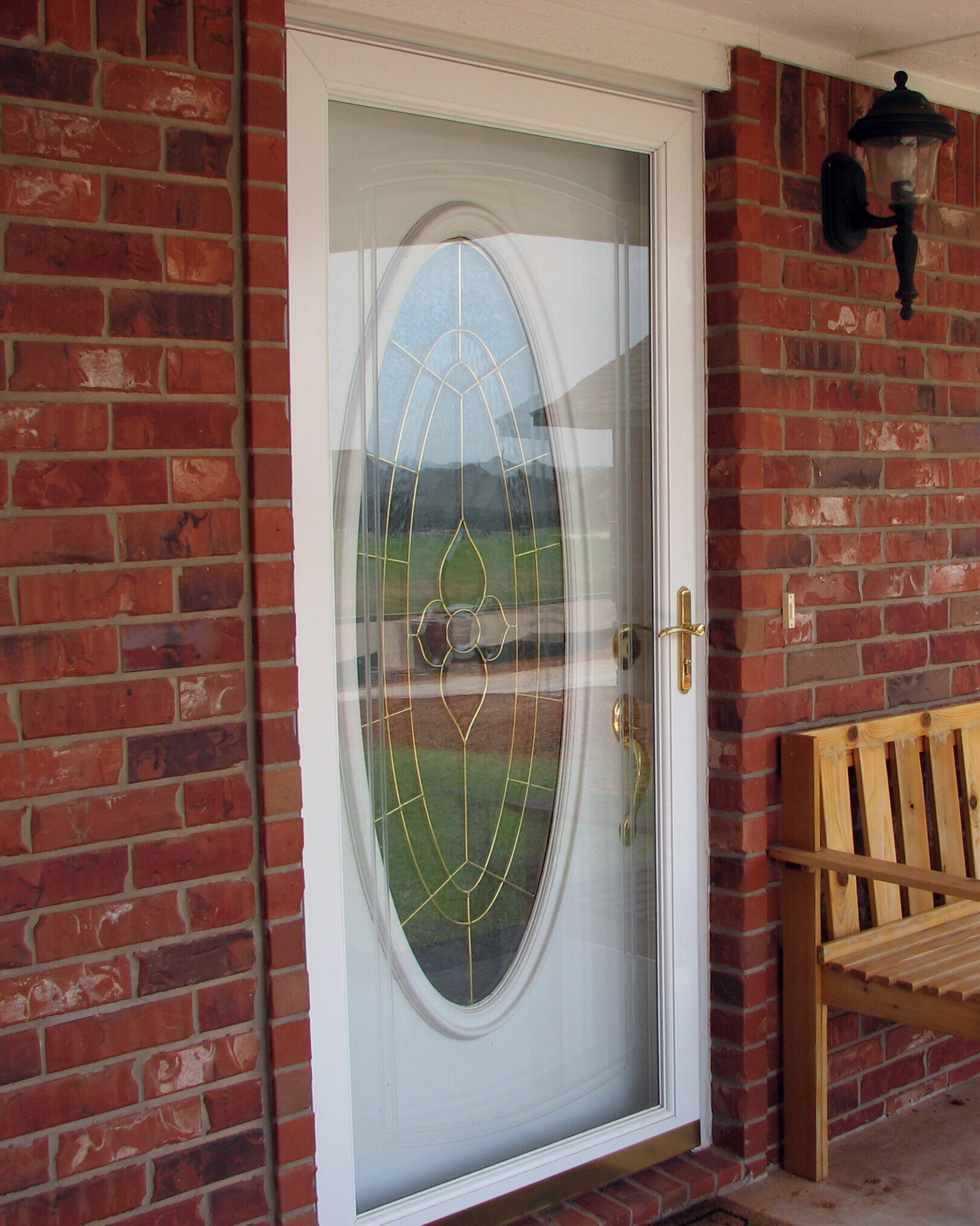 Custom Storm Door Installation Denver CO White storm door with oval decorative glass insert installed on a brick home entryway in Denver, CO